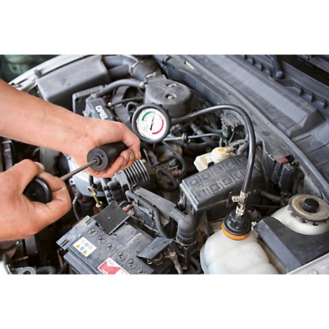 Eine Person überprüft den Motor eines Autos. Ein Messgerät wird gehalten, das auf dem Motor befestigt ist.